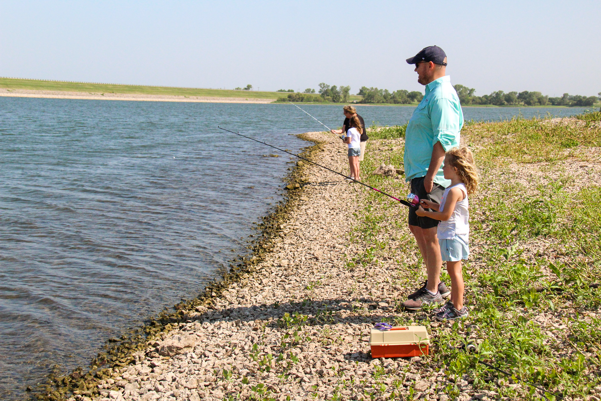 Jonathan Leeper looks across the water at Winfield City Lake beside his daughter Norah, while Nancy Vaught assists Mary Leeper in the background during the first annual Bass N’ BBQ kids’ fishing derby.
