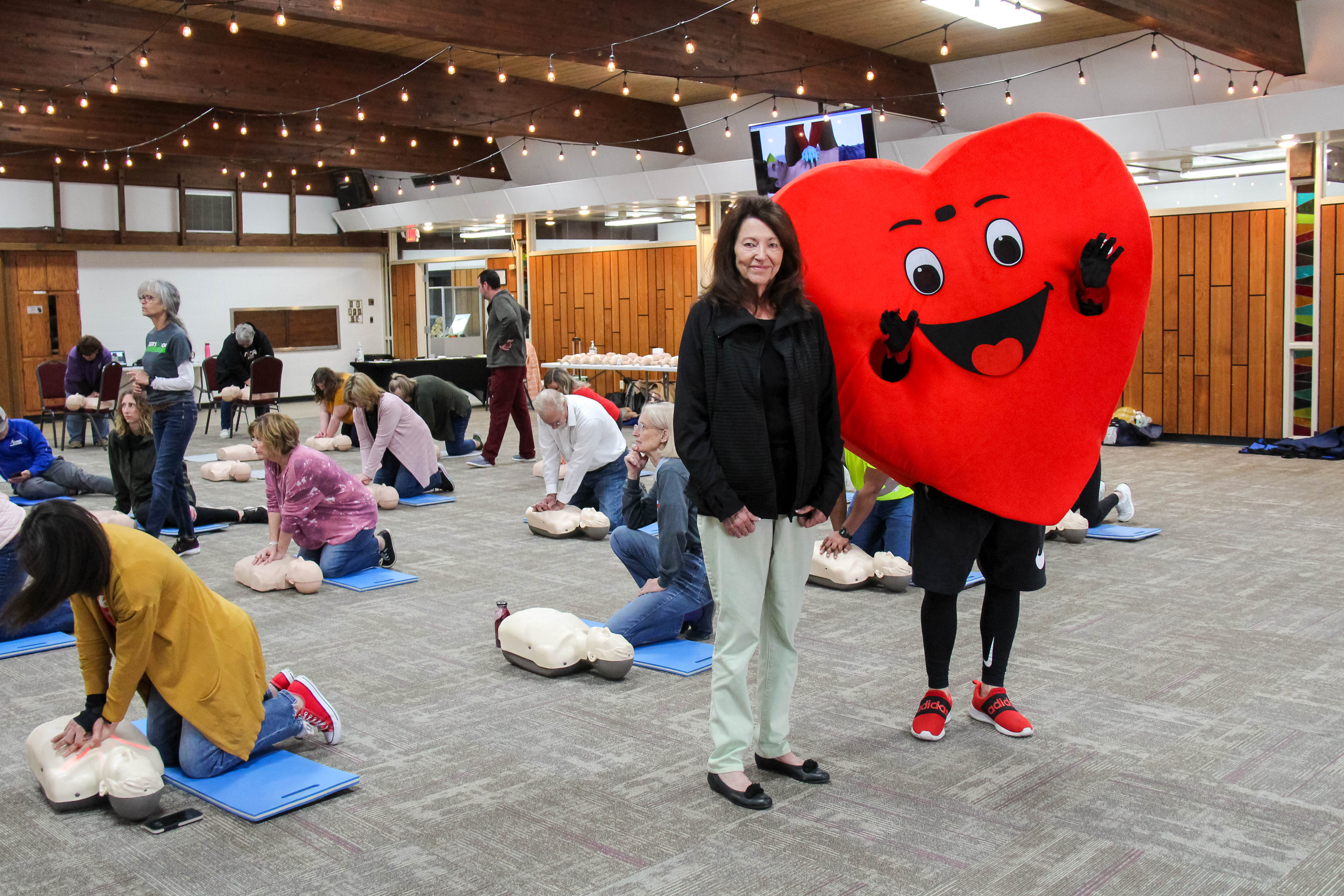 Standing with the Beats Go On mascot Willy, co-chair Paula Radcliff proudly hosts participants in the community-wide CPR training at Baden Square.